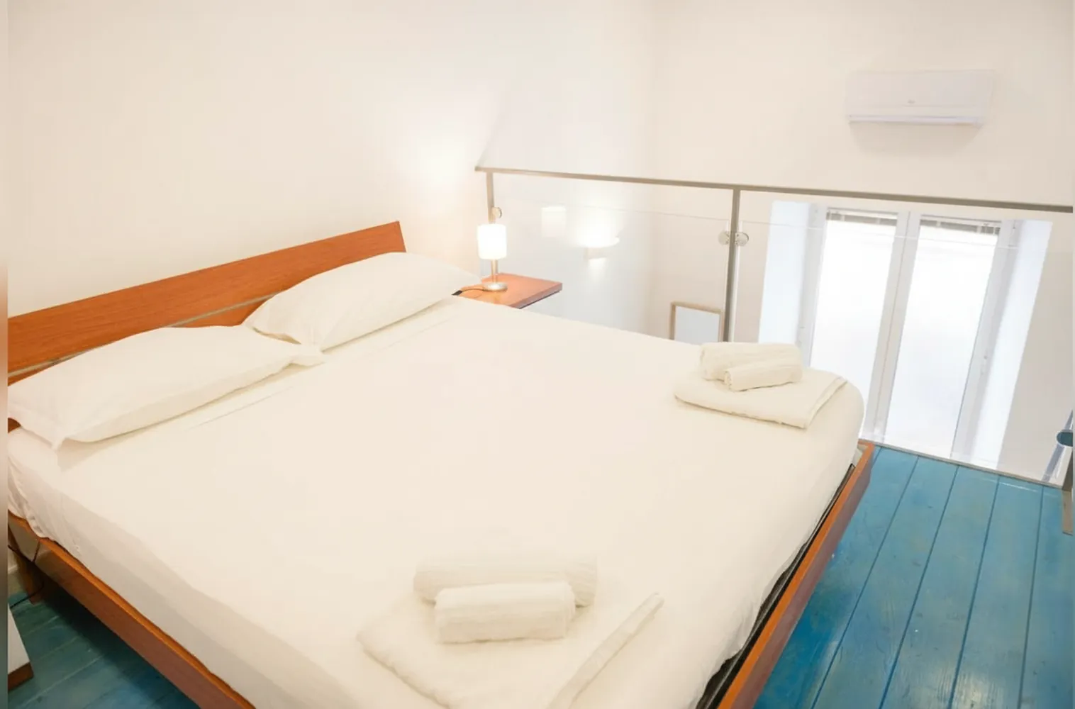 Il soppalco con il letto matrimoniale, i comodini e la ringhiera in vetro verso la finestra